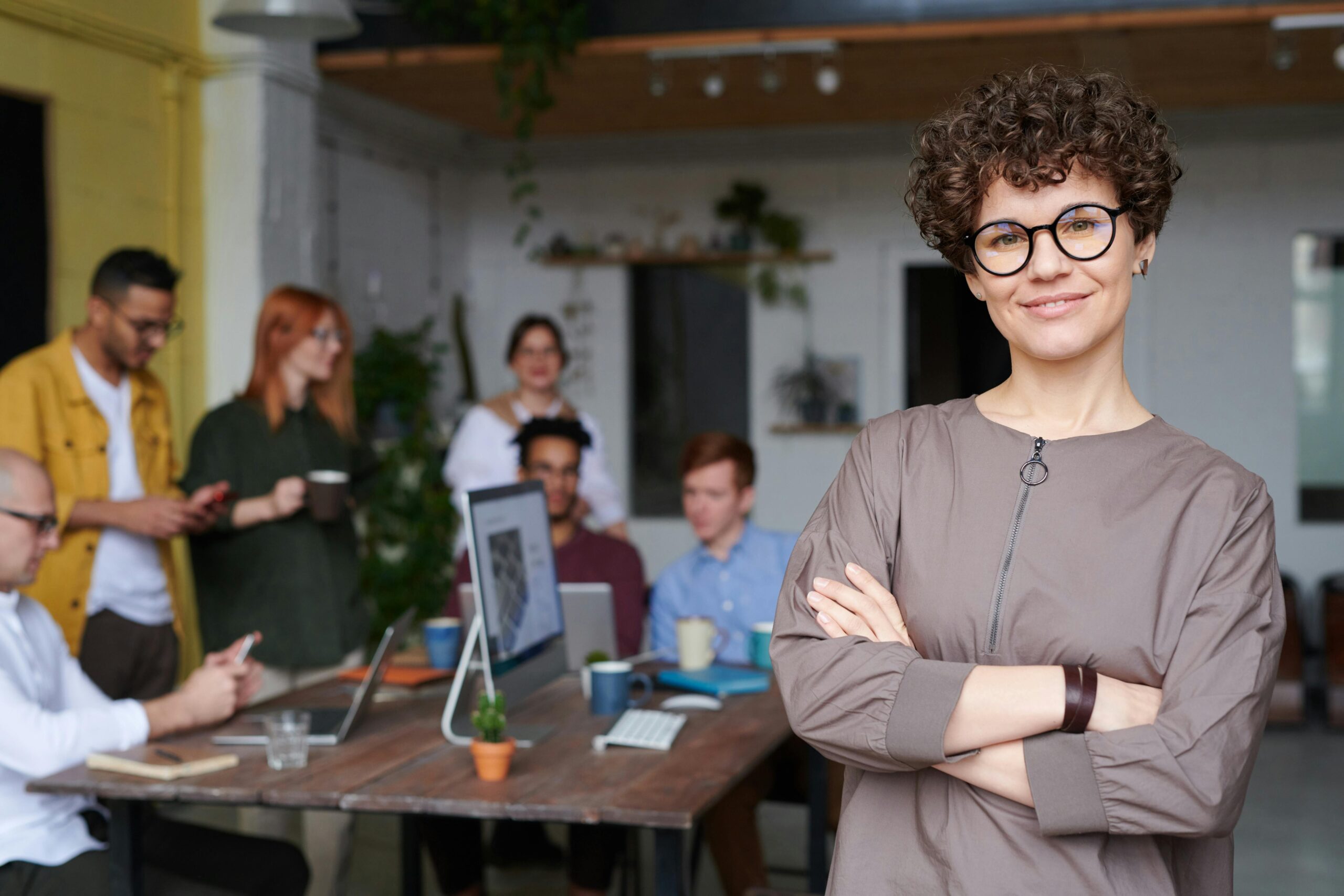 A woman in a modern office with coworkers behind her.